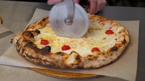 Closeup of a Chef Cutting a Pizza with Cheese and Tomatoes with a Special Knife