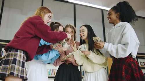 Grupo de cinco estudantes multirraciais contando dinheiro juntas em uma biblioteca moderna durante