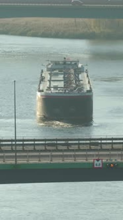 Crude oil tanker approaches industrial port under a bridge on a calm river while fueling global