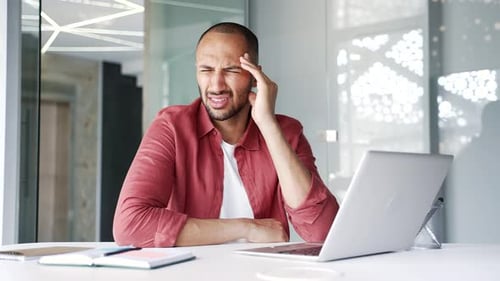 Man with Headache Rubs Temple in Office