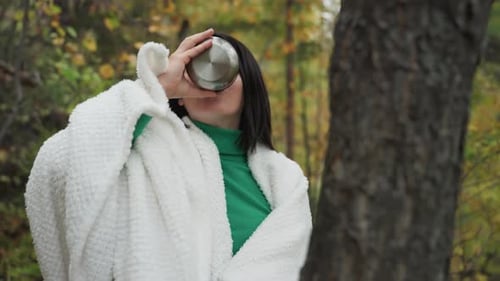 Woman Drinking from Thermos in Autumn Forest