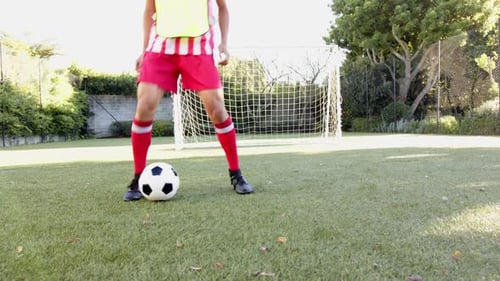 Playing soccer, athlete in red uniform dribbling ball on field near goal