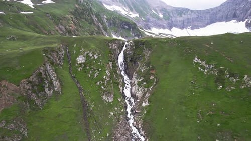 Waterfall flowing through a green mountain valley, surrounded by steep cliffs