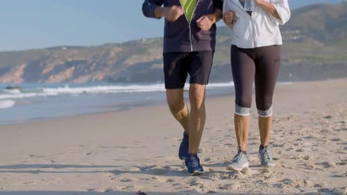 Elderly Couple in Sportswear Running on Sandy Beach Together