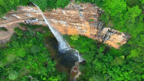 Drone captures majestic waterfall cascading from cliff.