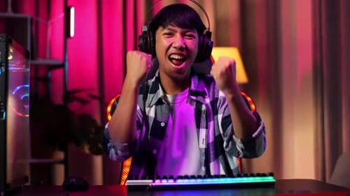Front View Of Excited Asian Teen Boy Gamer Celebrates Victory While Playing Video Game On Computer