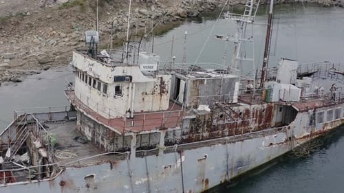 Rostgraues, halb untergetauchtes Schiffswrack, das an einem bewölkten, bewölkten Tag in Küstennähe vor Anker lag. Langsamer Luftbild