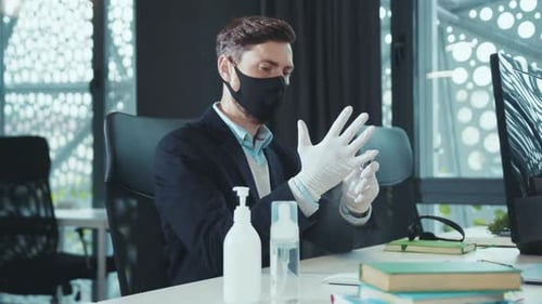 Suited Man Sanitizes Gloves in Office with Mask