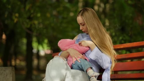 Mother Breastfeeding Infant on Park Bench in Daylight