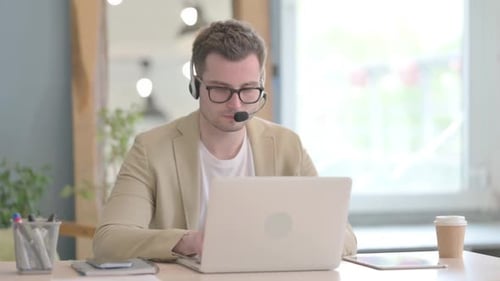 Young Man Working At Computer Wearing Headset