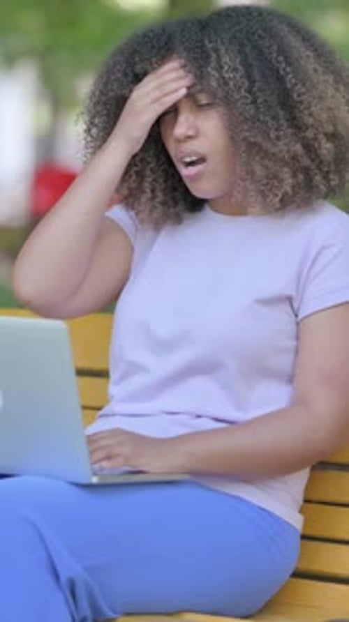 Woman using laptop on bench gets a headache
