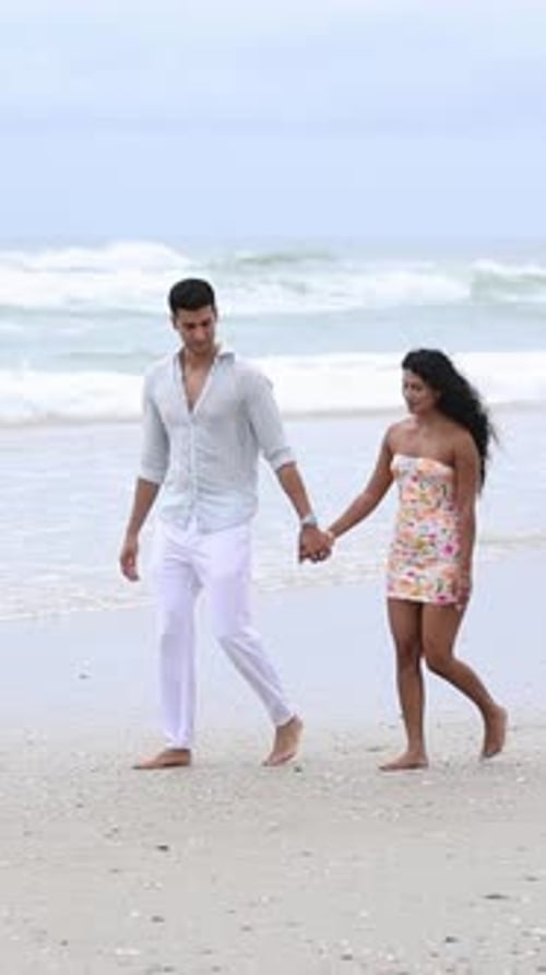 Romantic Young Couple Walking Hand in Hand on a Beach