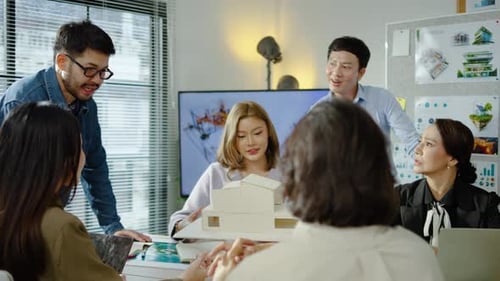 Architects and designers work presenting and discussing house model in office meeting.