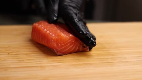 Close-up of a chef slicing fresh salmon on a wooden cutting board.
