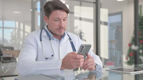 Middle Aged Doctor Using Smartphone in Clinic