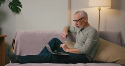 Senior Man Using Laptop on Sofa at Home