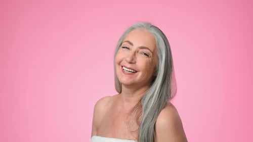 Elderly Woman With Gray Hair Smiles Against a Pink Background in Studio Setting