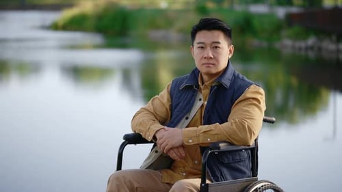 Serious Asian Disabled Man Sitting on the Wheelchair on the Pier in the Local Lake Looking at the