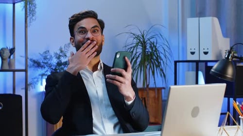 Young Adult Celebrates Success With Phone in Office