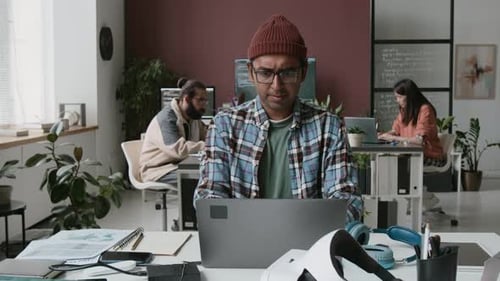 Stirnrunzelnder indischer männlicher Softwareentwickler codiert auf Laptop im Büro