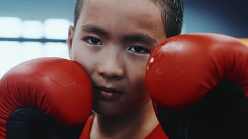 Nahaufnahme eines jungen asiatischen Jungen, der kampffähig in die Kamera schaut und ein rotes T-Shirt trägt