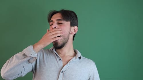Young Adult Man Yawning Against a Green Background