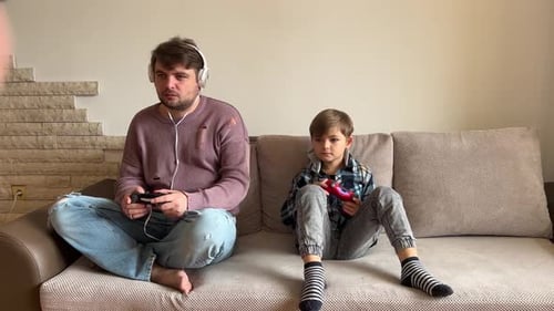 Father And Son Sitting On Sofa In Lounge Playing Video Game