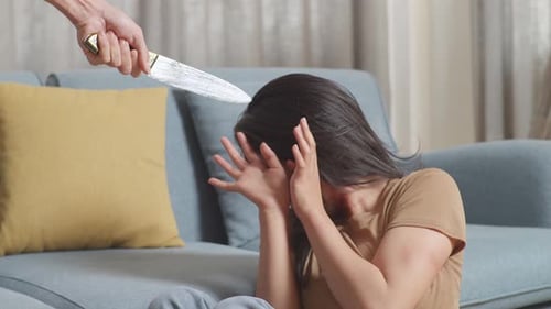 Woman Victim Of Violence Sits On The Floor Being Scared Of A Man Holding A Knife Threatening Her