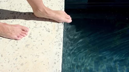 Bare feet are poised on the edge of a swimming pool, ready to dip into the water