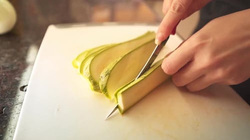 Female hands slicing a green zucchini in the kitchen in slow motion