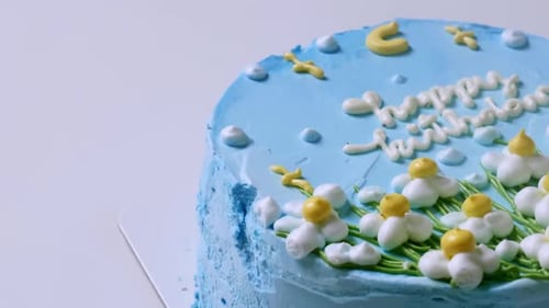 Close-up shot of the top of a birthday cake with blue frosting and decorated with white and yellow f