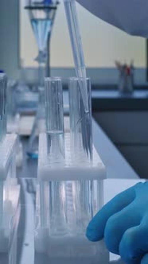 Close Up of Chemist Pouring Blue Liquid Into Test Tubes with Pipette for Analysis