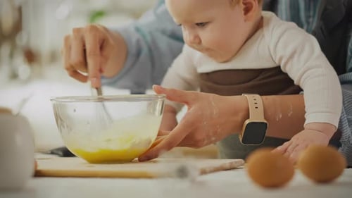 A young mother in modern clothes carefully beats eggs for baking pancakes in the home kitchen