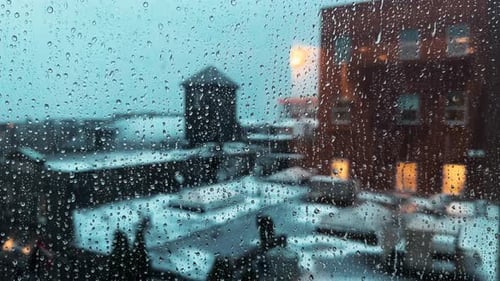 Raindrops Flow Down the Window Glass Against the Backdrop of the Night City
