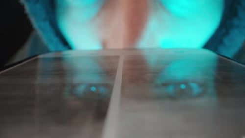 In the darkness and under dim blue light, a man in a hoodie quickly browses videos on the Internet