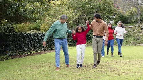 Ao ver o avô e o pai balançando as mãos da criança, família extensa passeando no gramado apontando para frente
