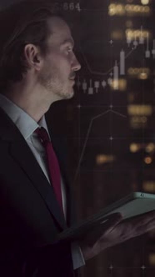Businessman Working Late Looking at Digital Tablet in Office with Graph and Skyline