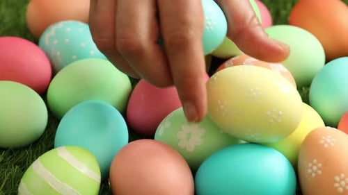 Woman putting decorated Easter eggs on green grass outdoors, closeup