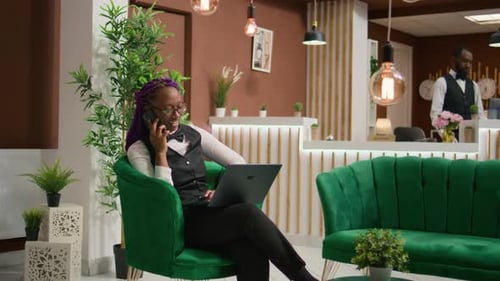 Smiling Woman Using Phone and Laptop in Hotel Lobby