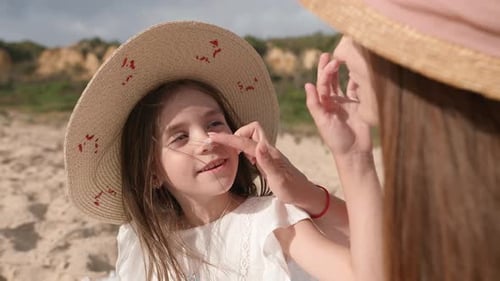 The Mother and Daughter are Placed on a Blanket at the Beach and Given Cream on Their Noses