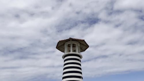 Black and white striped lighthouse with cloudy sky in the background. Low angle