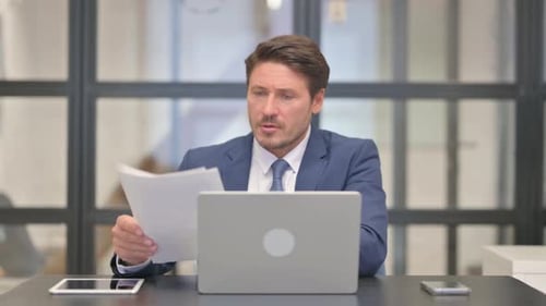 Man Works at Desk with Laptop and Paper
