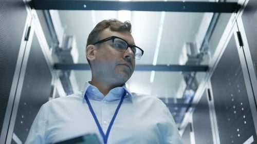 Server Technician Working in Data Center. They Walk Through Working Rows of Server Racks.