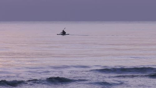 Man paddles kayak on calm sea at dawn, silhouette, slow motion