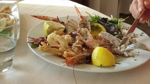Close up on woman hands cutting fish fillet on mix grilled seafood plate