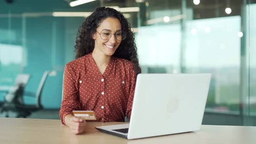 Glückliche junge Geschäftsfrau beim Online-Shopping und tippt im Sitzen Kreditkartendaten auf dem Laptop ein