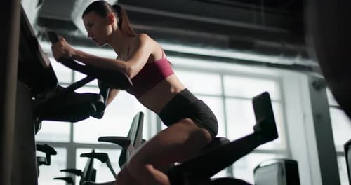 A Young Beautiful Brunette Girl in Sportswear Exercises on a Simulator in the Gym Doing Cardio
