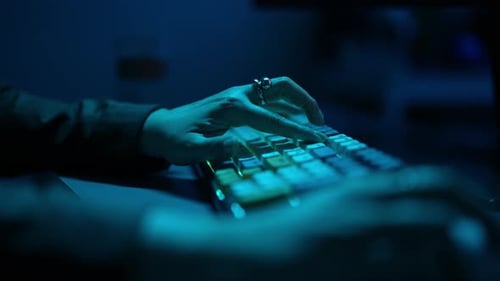 Woman Typing on Illuminated Keyboard in Dark Room