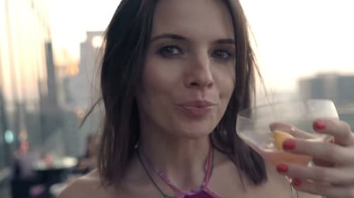Happy young woman enjoying a delicious cocktail on a luxurious city rooftop terrace