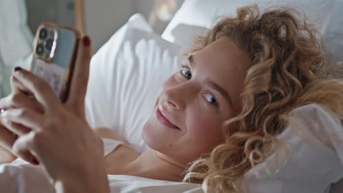 Pretty Woman Messaging Mobile Phone in Bed Closeup Smiling Happy Girl Resting